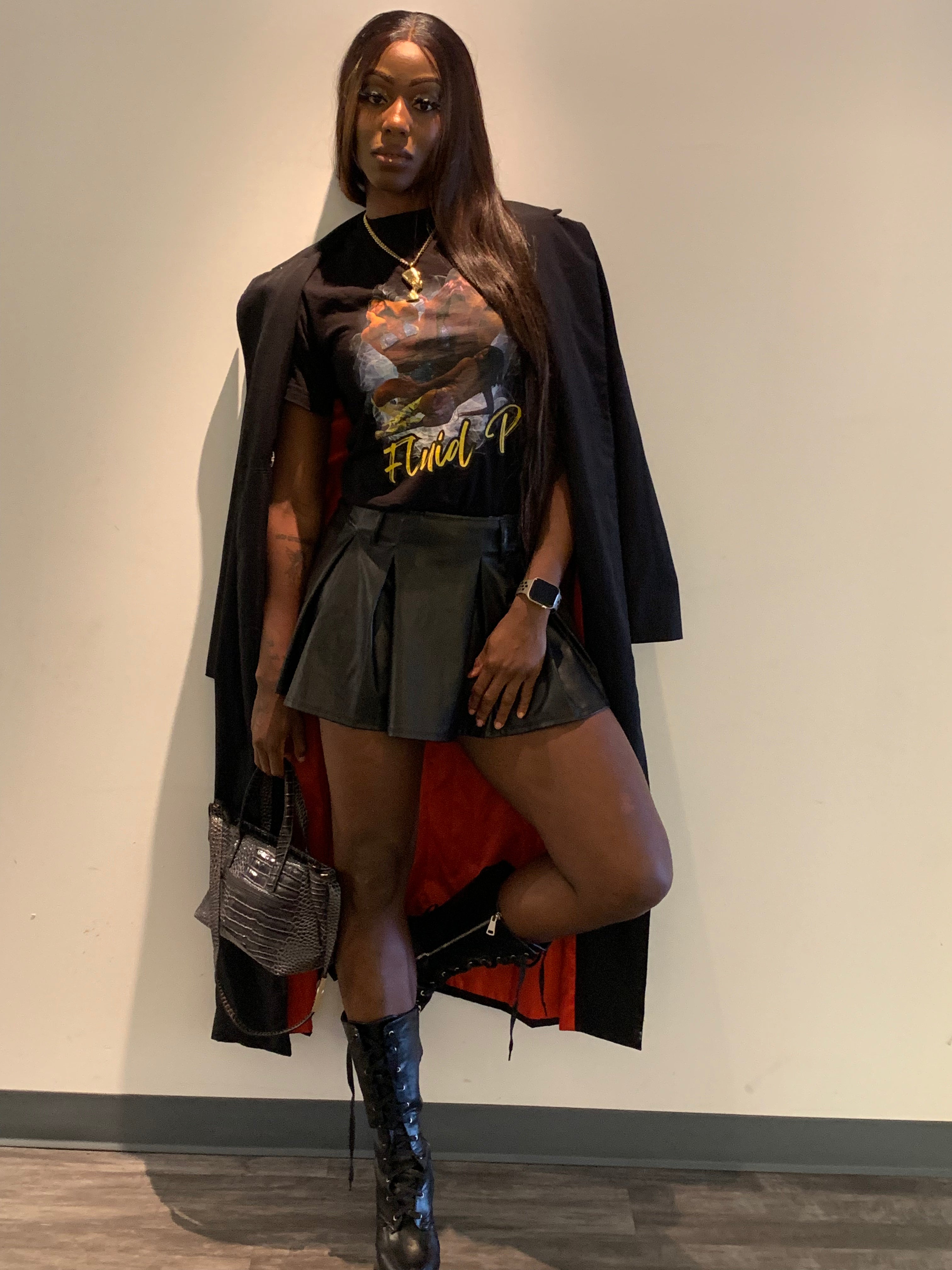 Woman wearing a graphic t-shirt, skirt, and coat against a plain wall.